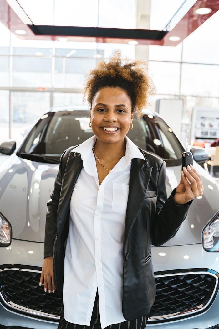 Smiling woman in a car dealership holding keys to her new vehicle.